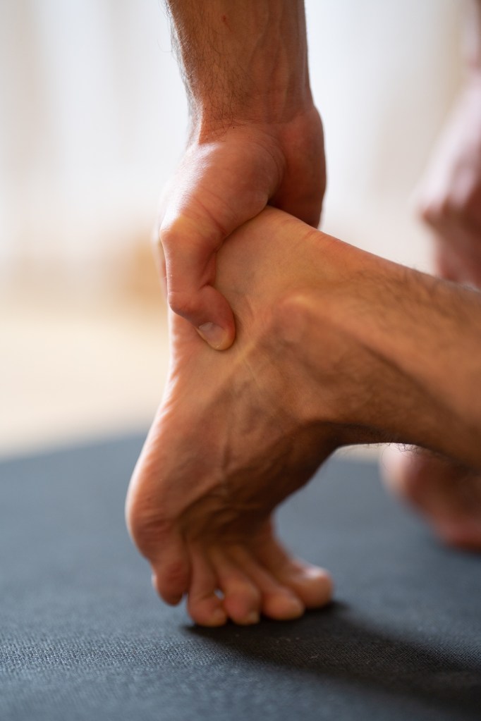 Man holding his heel because of pain, close-up, vertical